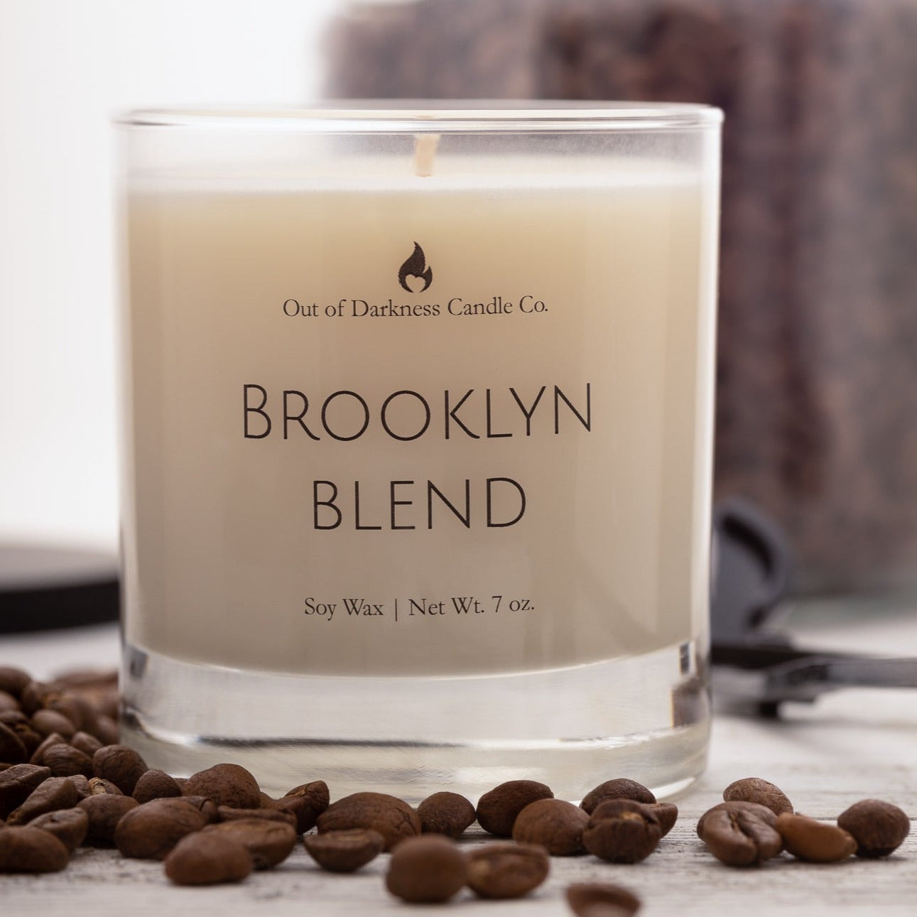 A glass jar candle that says Brooklyn Blend surrounded by coffee Beans