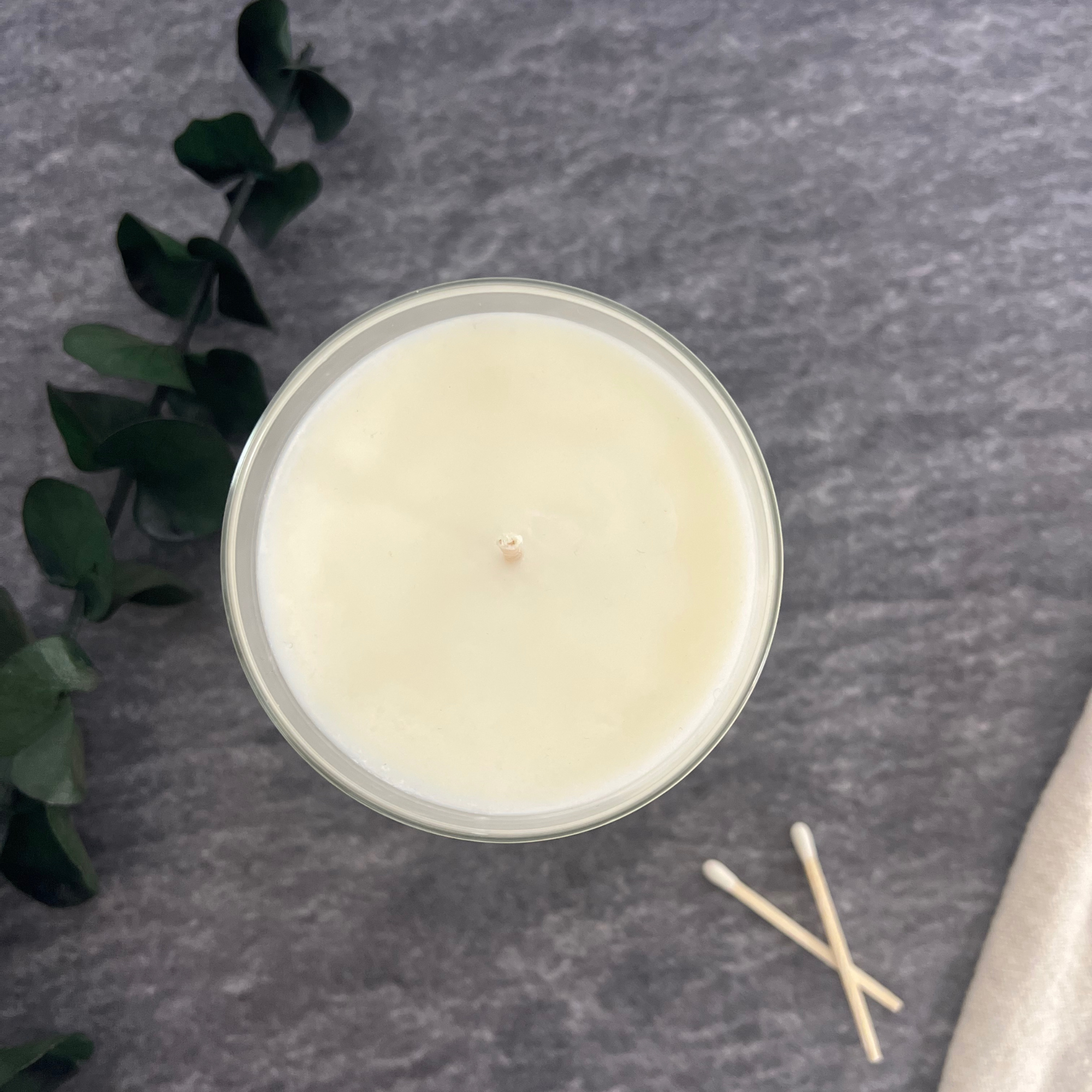 The smooth top of a soy wax candle with a sprig of eucalyptus and two wooden matches