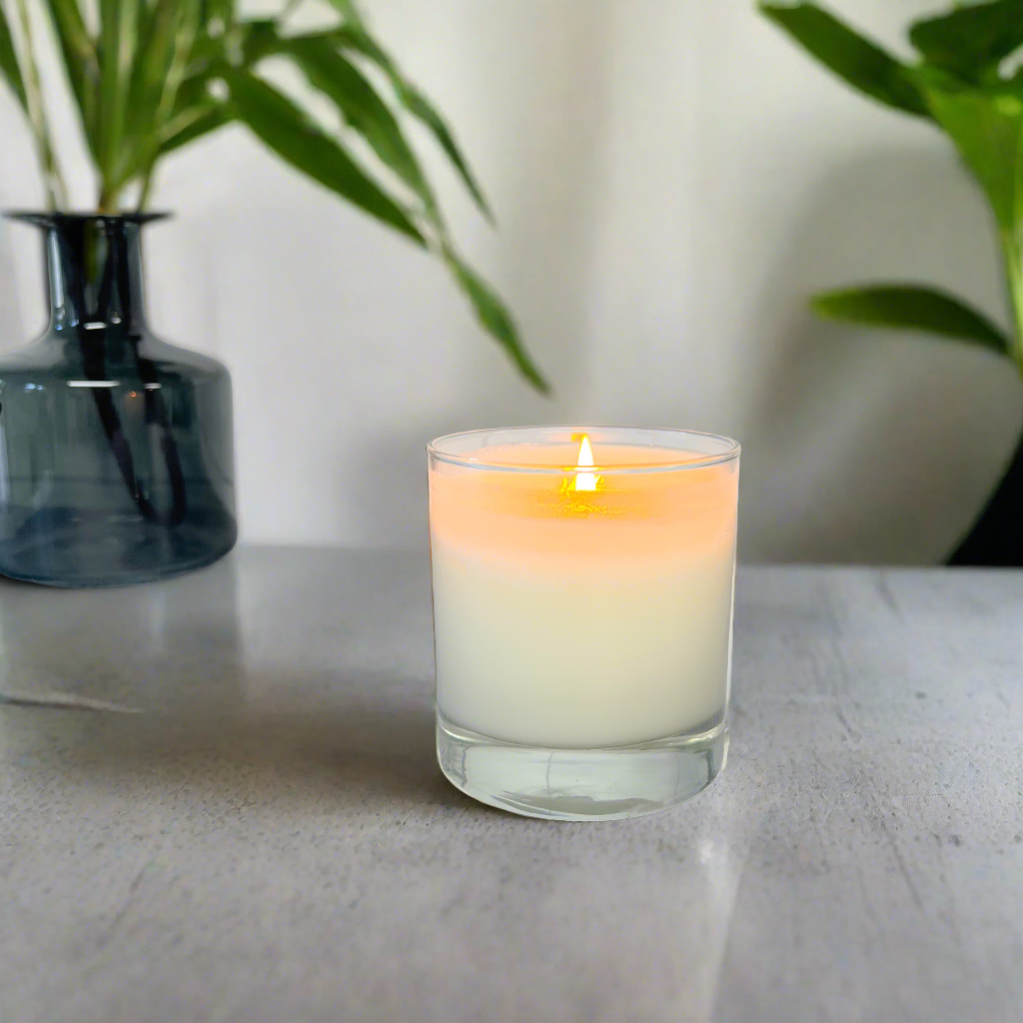 Unscented Soy Candle- sitting on a table with plants behind it