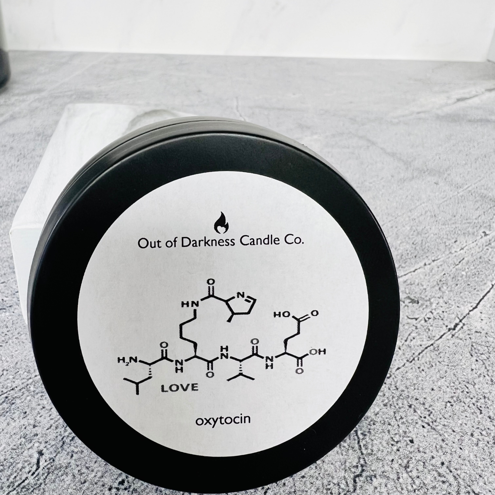 black tin with white label that shows the molecule for oxytocin and says Love on a gray background