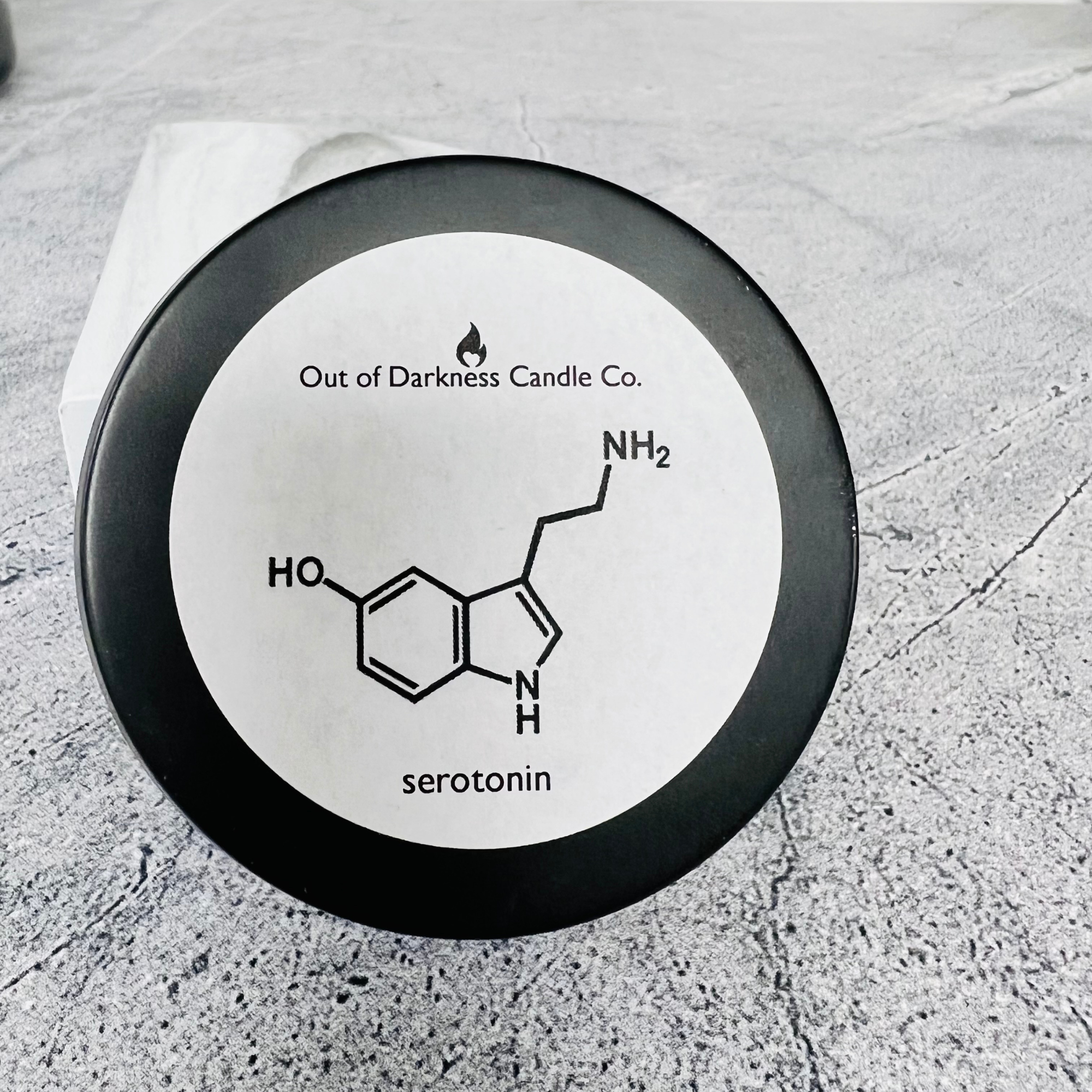 black tin candle with white label showing serotonin molecule