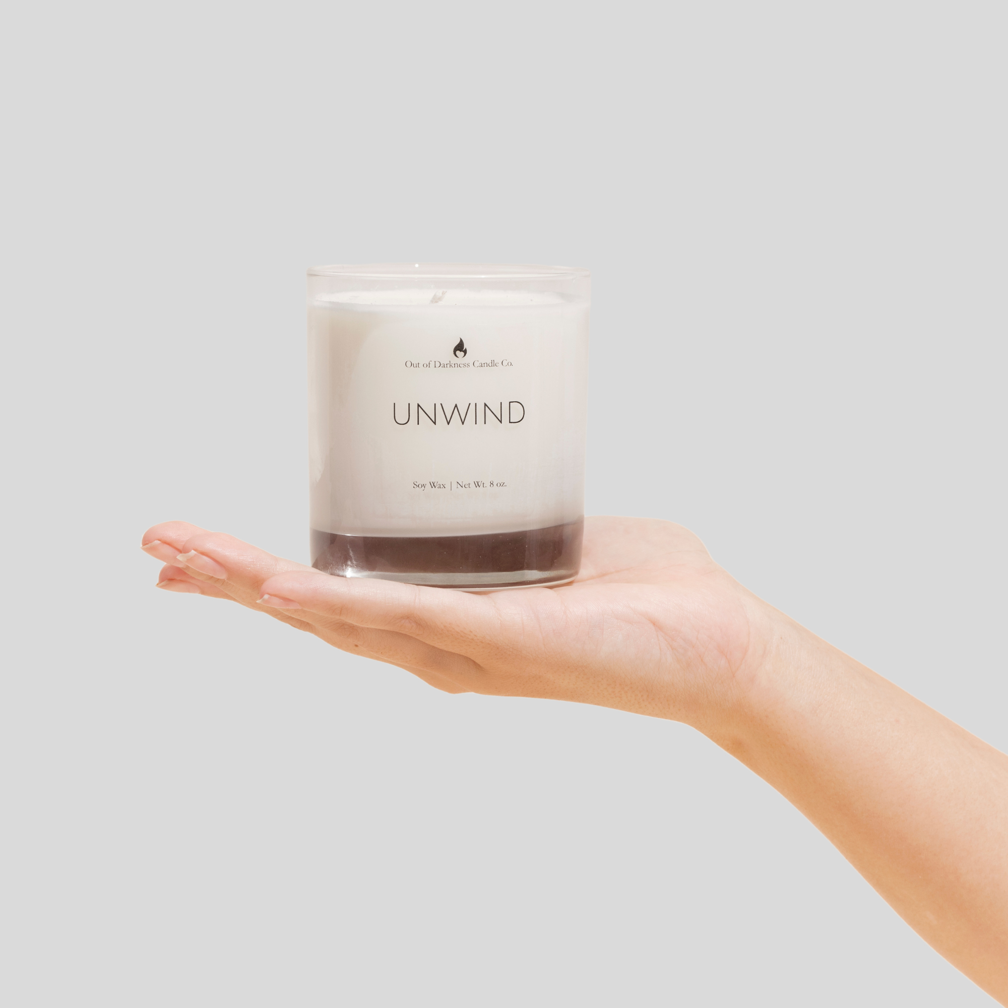 clear glass jar candle says unwind being held up by hand